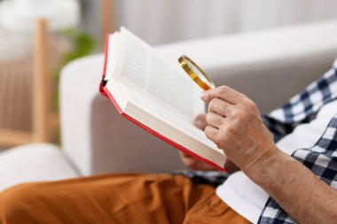 Üst düzey bir adam kanepede kitap okurken büyüteç kullanıyor.
