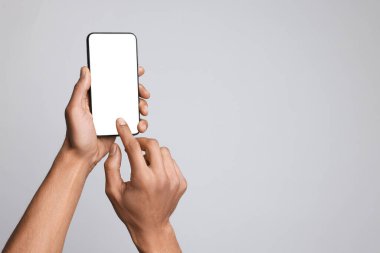 Açık gri arka planda boş ekranlı akıllı telefon tutan adam, yakın plan. Tasarım için model
