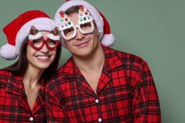 Noel Baba şapkalı mutlu çift, komik gözlükler ve gri yeşil arka planda pijamalar. Noel atmosferi