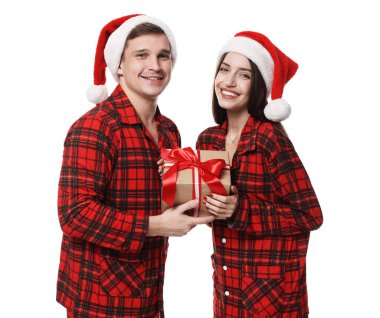 Noel Baba şapkalı ve pijamalı mutlu çift ve beyaz arka planda Noel hediyesi.