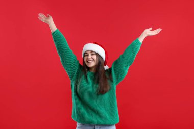 Kırmızı arka planda Noel Baba şapkalı heyecanlı kadın. Noel sezonu