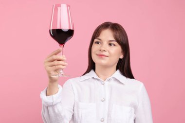 Profesyonel şarap garsonu, pembe arka planda bir bardak kırmızı şarap.