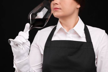 Profesyonel şarap garsonu siyah arka planda kırmızı şarap tadıyor, yakın plan.