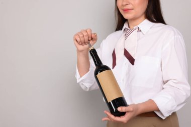 Profesyonel şarap garsonu açık gri arka planda şarap şişesi açıyor, yakın plan. Metin için boşluk