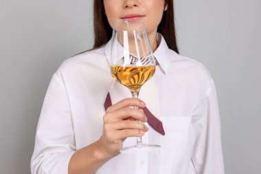 Profesyonel şarap garsonu açık gri arka planda beyaz şarap tadıyor. Yakın plan.