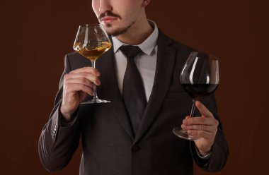 Profesyonel şarap garsonu kahverengi arka planda şarap tadıyor.