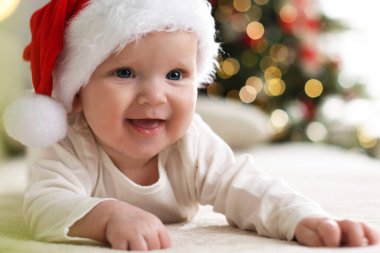 Noel Baba şapkalı şirin bir bebek Noel ışıklarına karşı kanepede, bokeh etkisi