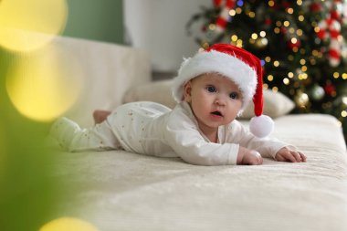 Noel Baba şapkalı şirin bir bebek Noel ışıklarına karşı kanepede, bokeh etkisi