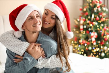 Pijamalı mutlu çift ve Noel için dekore edilmiş Noel Baba şapkaları. Metin için boşluk