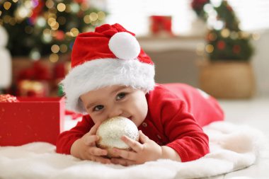 Noel Baba şapkalı şirin çocuk. Evde yerde süs eşyası var. Bebeğin ilk Noel 'i