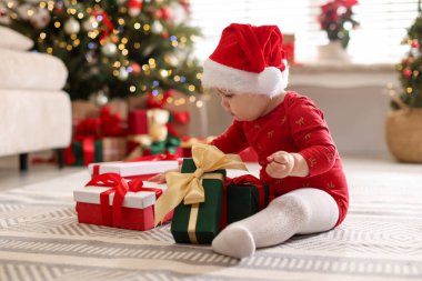 Evde yerde hediyeleri olan Noel Baba şapkalı şirin bir çocuk. Bebeğin ilk Noel 'i