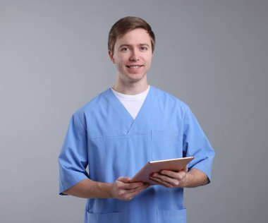 Gri arkaplanda tableti olan bir tıp asistanı portresi