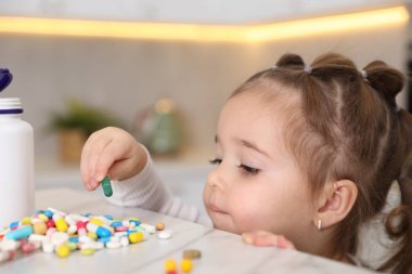 Evde çocuk güvenliği. Küçük kız mutfaktaki masada haplarla oynuyor, yakın plan.