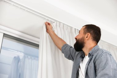 Evde pencere perdelerini asan adam, düşük açılı görüntü.