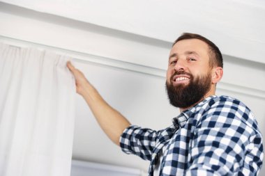 Evde pencere perdelerini asan adam, düşük açılı görüntü.