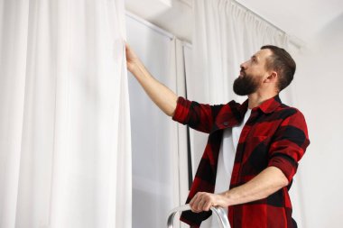 Evde perdeleri asan merdivenli bir adam var. Düşük açılı. Metin için boşluk