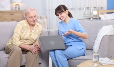 Huzurevinde yaşlı bir kadına dizüstü bilgisayar kullanmayı öğreten bakım işçisi.