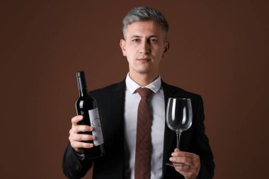 Kahverengi arka planda kırmızı şarap ve cam şişesi olan profesyonel şarap garsonu.