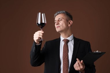 Kahverengi arka planda bir bardak kırmızı şarap ve panosu olan profesyonel şarap garsonu.
