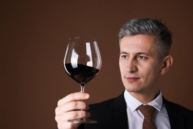 Kahverengi arka planda kırmızı şarap kadehi olan profesyonel şarap garsonu.