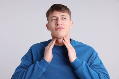 Açık gri arka planda boğaz ağrısı çeken hasta genç bir adam. Soğuk Semptom