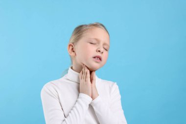 Açık mavi arka planda boğaz ağrısı çeken küçük bir kız. Soğuk Semptom