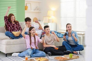 Video oyunu oynayan ve evde abur cubur yiyen bir grup genç.