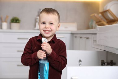 Evde çocuk güvenliği. Mutfakta bir şişe temizlik malzemesi olan küçük çocuk, mesaj için yer var.