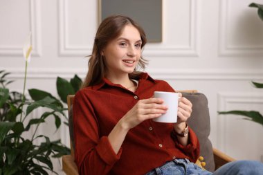 Evdeki koltukta bir fincan aromatik kahveli kadın.