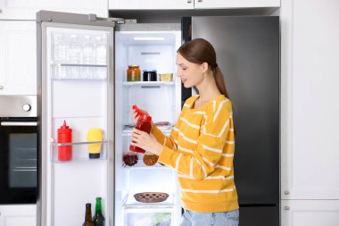 Mutfakta soslu kadın açık buzdolabının yanında.