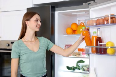 Kadın mutfaktaki buzdolabından portakal suyu alıyor.