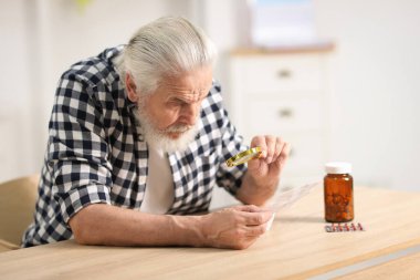 Ahşap masada ilaç öğretirken büyüteç kullanan kıdemli bir adam.