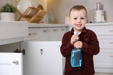 Evde çocuk güvenliği. Mutfakta bir şişe temizlik malzemesi olan küçük çocuk, mesaj için yer var.