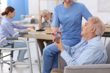 Huzurevindeki yaşlı kadına bir bardak su veren bakım görevlisi, yakın plan.