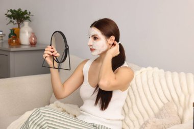 Yüzünde kozmetik ürünler olan bir kadın aynaya bakıyor.