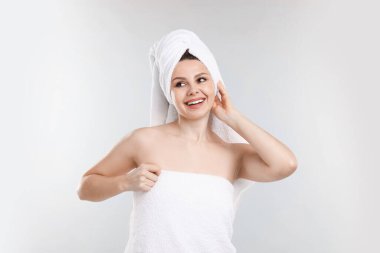 Açık gri arka planda, havluya sarılı saçları olan bir kadın.