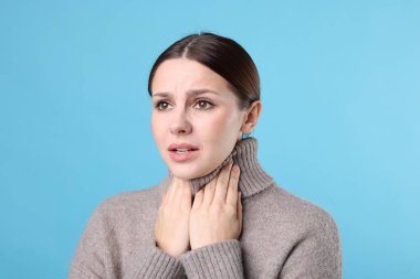 Açık mavi arka planda boğaz ağrısı çeken bir kadın. Soğuk Semptom