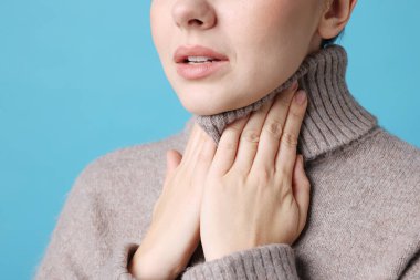 Açık mavi arka planda boğazı ağrıyan bir kadın, yakın plan. Soğuk Semptom