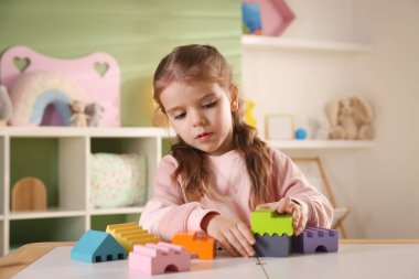 Küçük kız oyun odasındaki beyaz masada oyuncaklarla oynuyor.