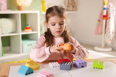 Küçük kız oyun odasındaki beyaz masada oyuncaklarla oynuyor.