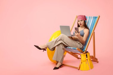 Akıllı telefonu, dizüstü bilgisayarı, şişirilebilir yüzüğü ve pembe arka planı olan yüzgeçleri olan bir ofis çalışanı. Metin için boşluk