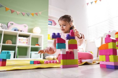 Oyun odasında yerde oyuncakla oynayan küçük kız, düşük açı.