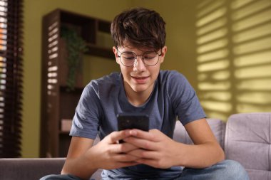 Genç çocuk evdeki kanepede akıllı telefon kullanıyor.