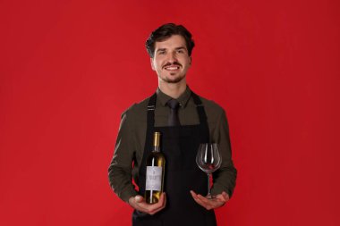 Kırmızı arka planda beyaz şarap ve cam şişesi olan profesyonel şarap garsonu.