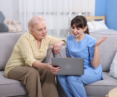 Huzurevinde yaşlı bir kadına dizüstü bilgisayar kullanmayı öğreten bakım işçisi.