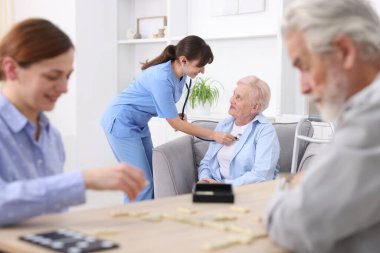 Masada yaşlı bir adamla domino oynayan ve hastasına huzur evinde yardım eden bir kadın.