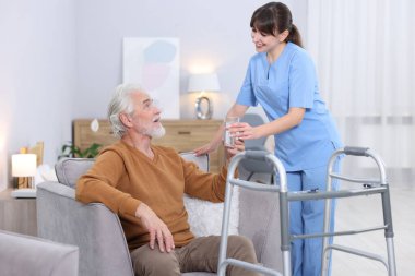 Bakım işçisi huzurevindeki yaşlı adama bir bardak su veriyor.