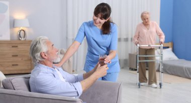 Bakım işçisi huzurevindeki yaşlı adama bir bardak su veriyor.