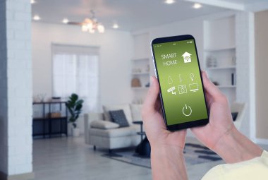 Akıllı ev sistemi. Oda özelliklerini kontrol etmek için cep telefonundaki uygulamayı kullanan kadın, yakın plan