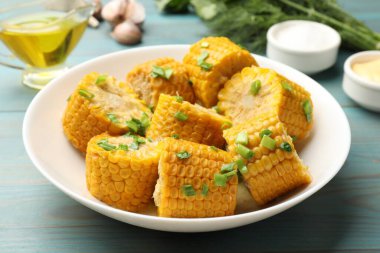 Kaynamış mısır koçanları açık mavi ahşap masada yeşil soğanlı, yakın plan.